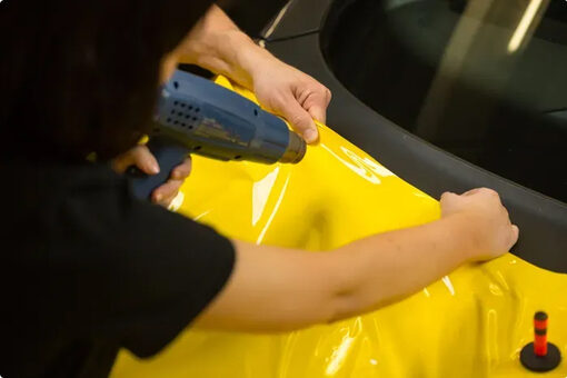 Installer heating yellow wrap vinyl onto a vehicle
